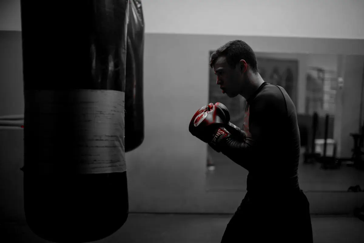 A boxer in red gloves trains alone beside a heavy bag